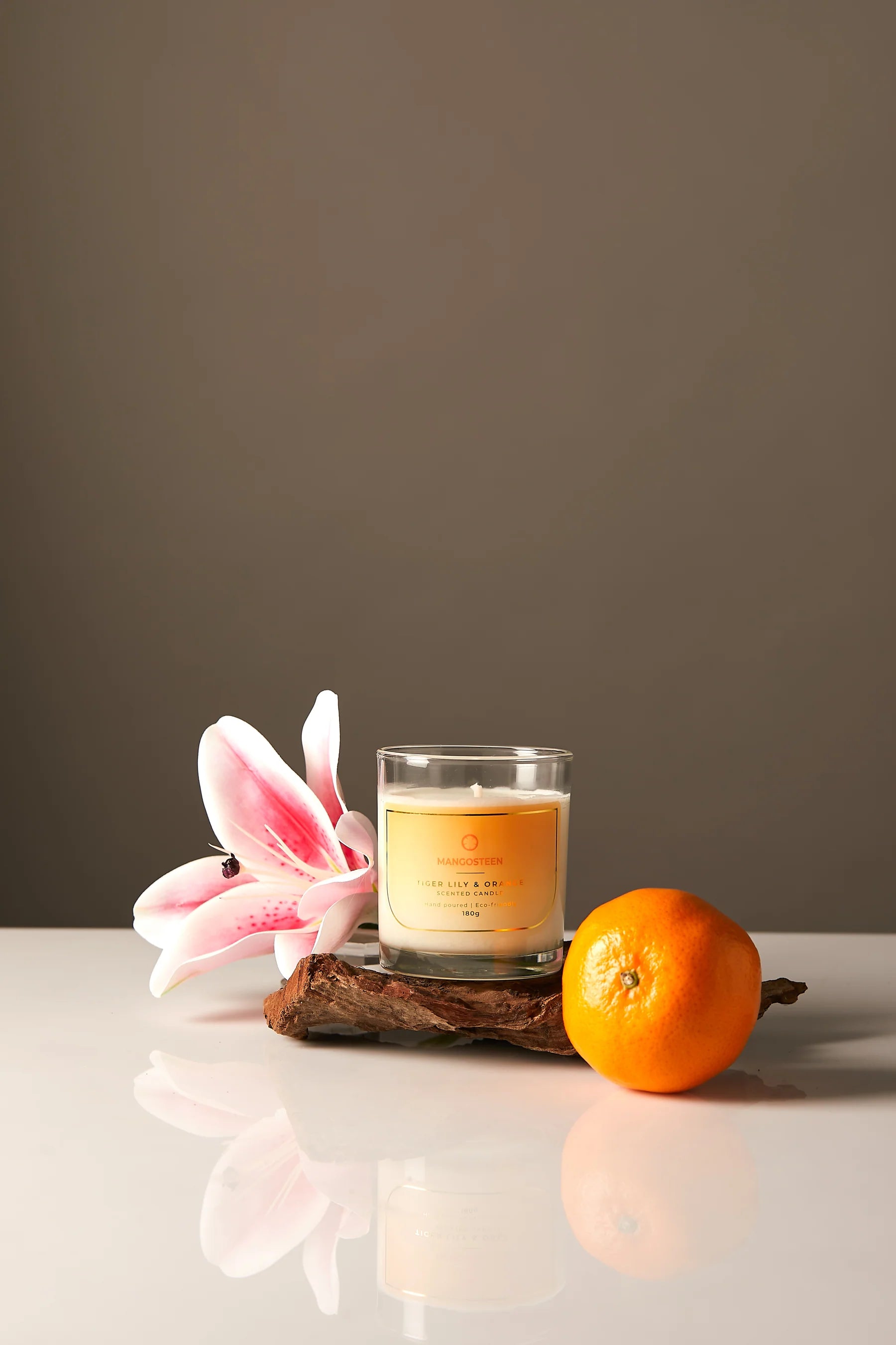 Candle in a glass jar with a floral and fruit decoration on a reflective surface.