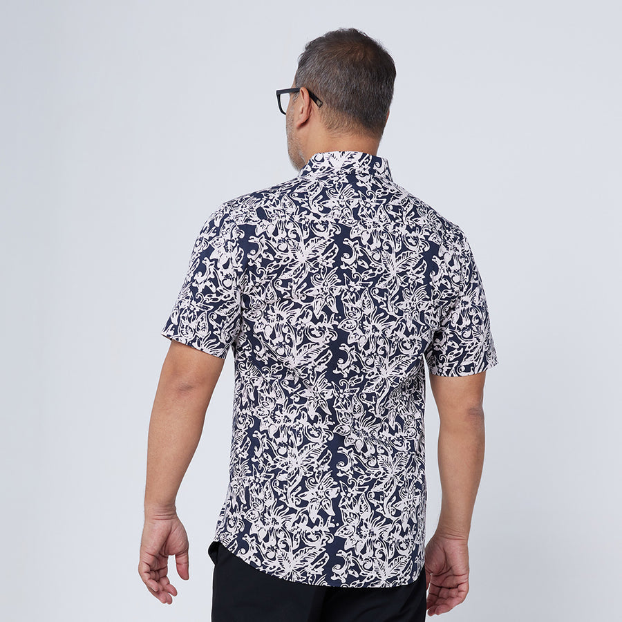 a model posing with his back on the camera to showcase the back of a batik shirt in the pattern black floret