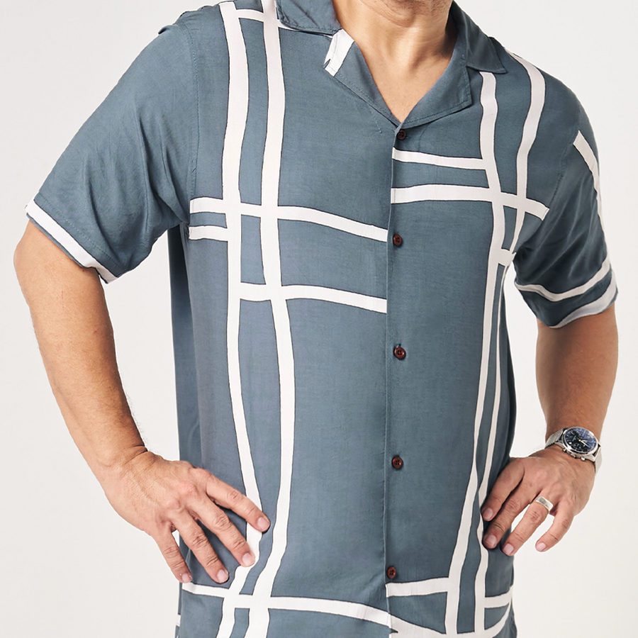 In a whitebox photo, a model elegantly poses while wearing a grey brush patterned batik shirt against a neutral background, showcasing the details on the shirt