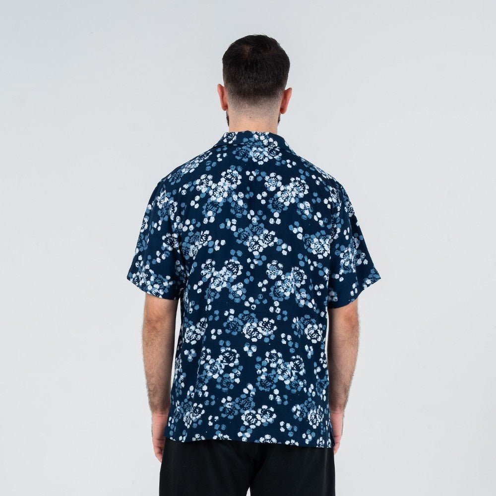 Back view of a man wearing the Men’s Cuban Shirt in Navy Blossom, a batik design featuring hand-painted floral motifs in shades of blue and white.