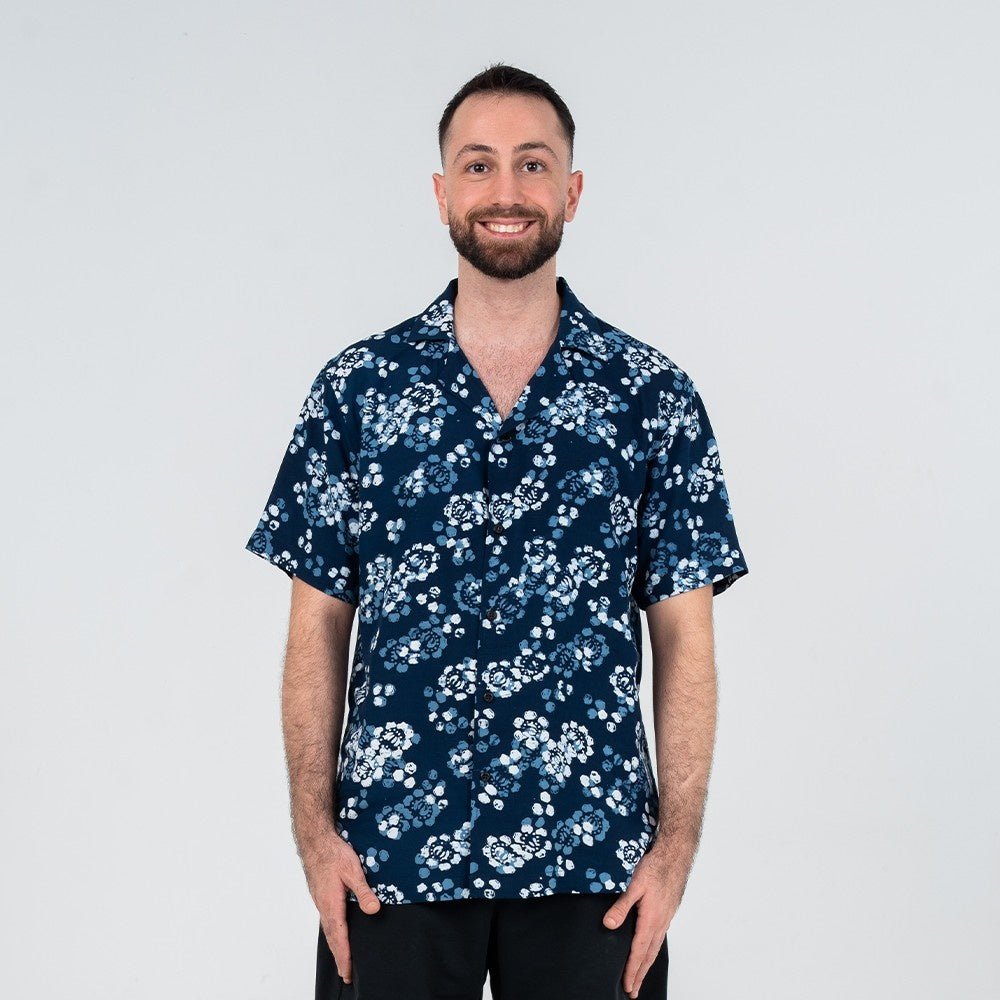 Front view of a man wearing the Navy Blossom Men’s Cuban Shirt, designed with a floral batik pattern in blue and white, short sleeves, and wooden buttons.