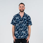 Front view of a man wearing the Navy Blossom Men’s Cuban Shirt, designed with a floral batik pattern in blue and white, short sleeves, and wooden buttons.