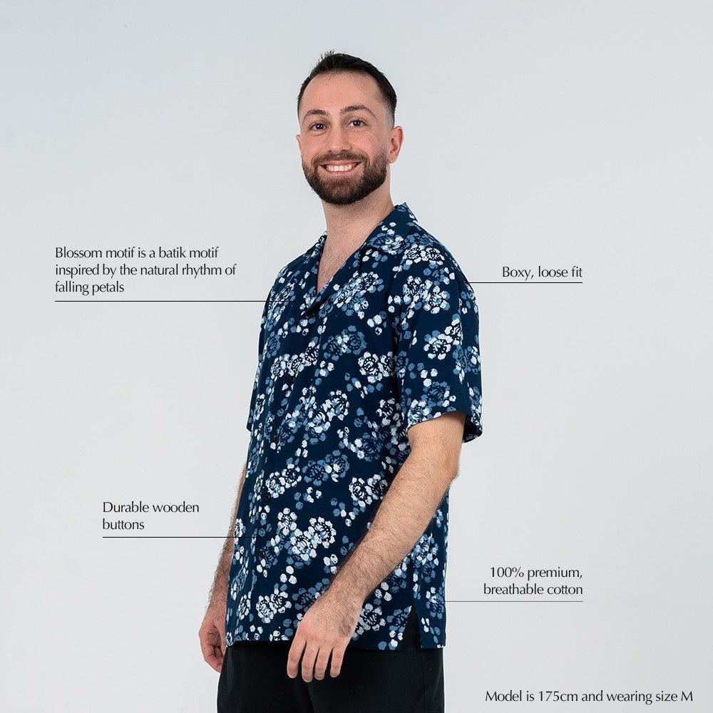Model wearing the Navy Blossom Men’s Cuban Shirt with callouts on the boxy loose fit, breathable cotton fabric, wooden buttons, and floral batik motif inspired by falling petals.