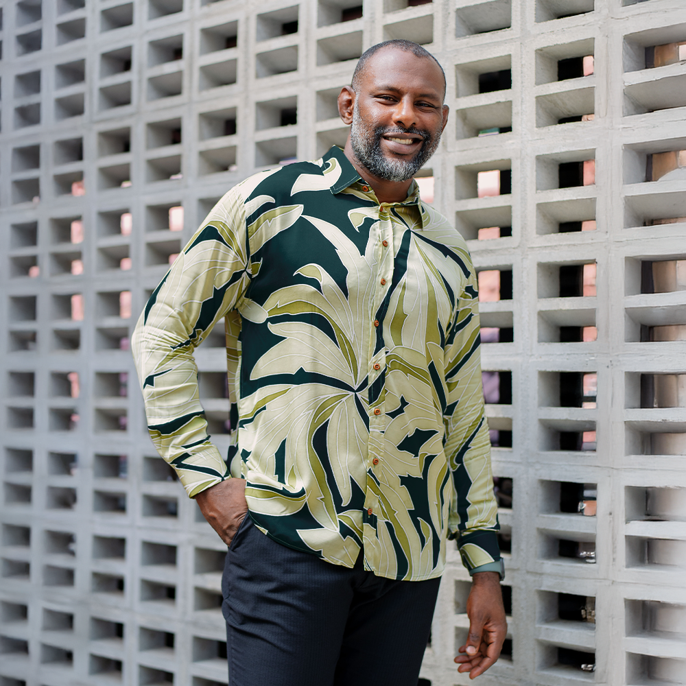Man wearing Forest Palma batik shirt styled for casual or workwear, standing against a textured wall.