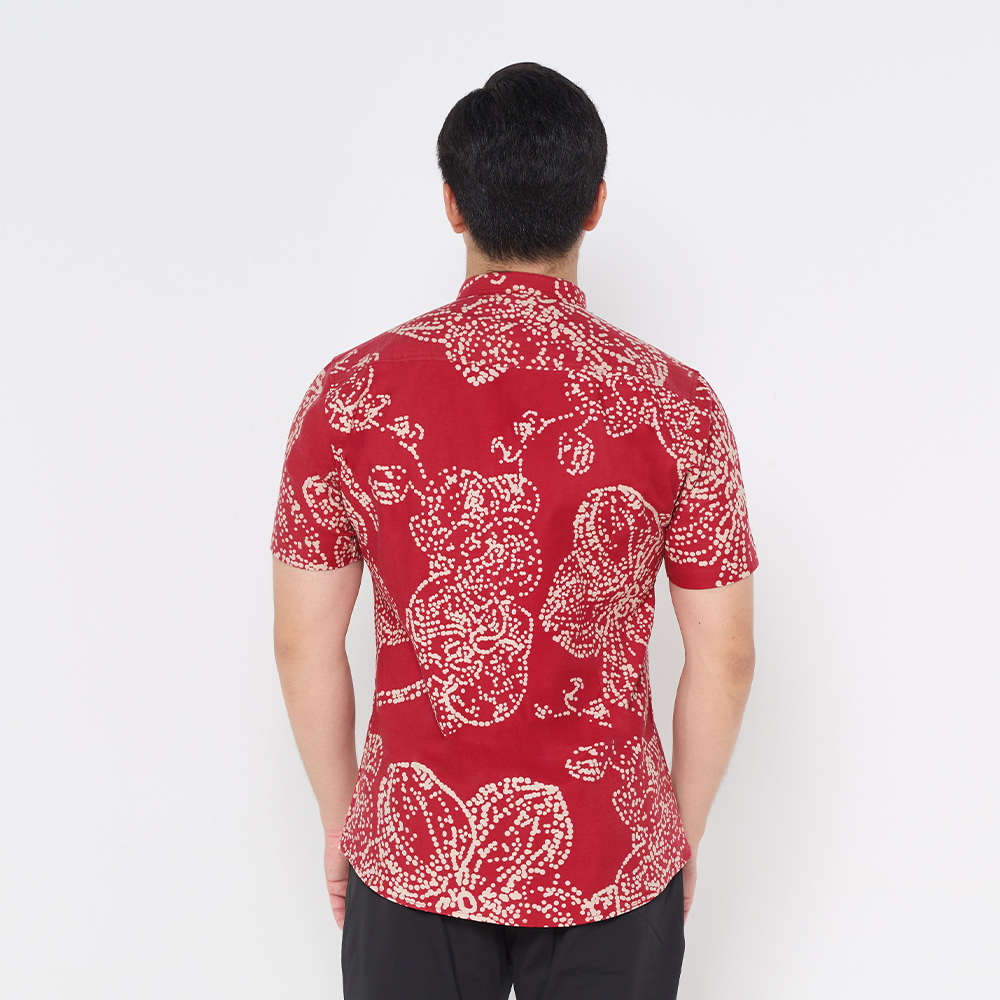 a man showcasing the details on the back of batik shirt in the pattern crimson orchid against a white background