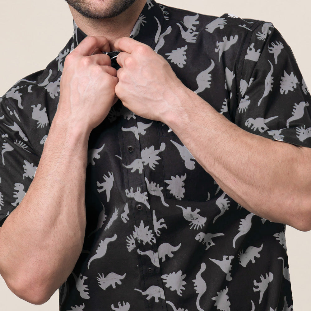 a close up photo of a man posing in front of a wall while wearing a dinosaur batik shirt in the color grey