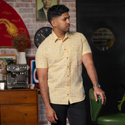 a man wearing a mustard arabesque batik shirt in a lifestyle photo while leaning against a green chair