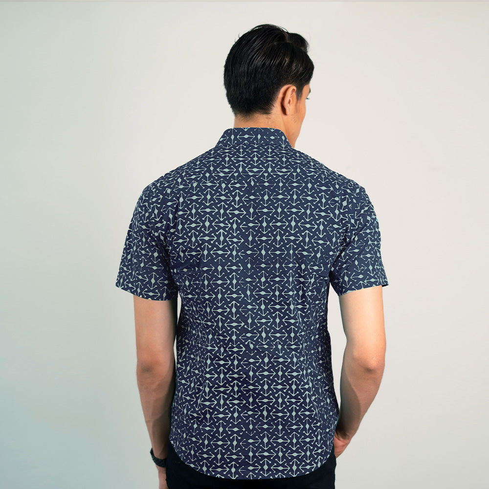 a back shot of a man standing in front of a white wall while wearing a batik shirt in navy kompas from batik boutique