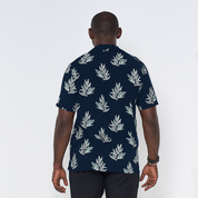 a man showcasing the details on a batik shirt in the pattern navy olive leaf against a white background