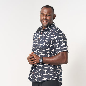 photo of man standing in front of white background wearing batik shirt in black colour and pattern inspired from airplane