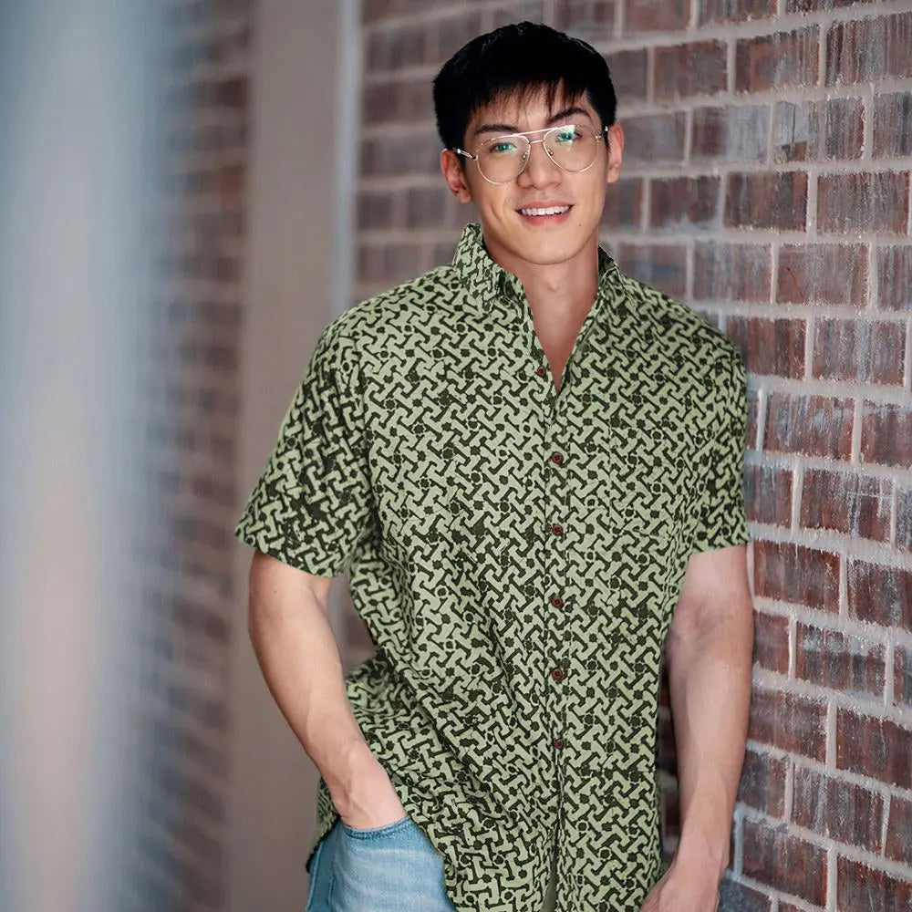 A captivating lifestyle image capturing a model's pose against a rustic brick wall, dressed in a striking batik shirt featuring the Forest Arabesque pattern