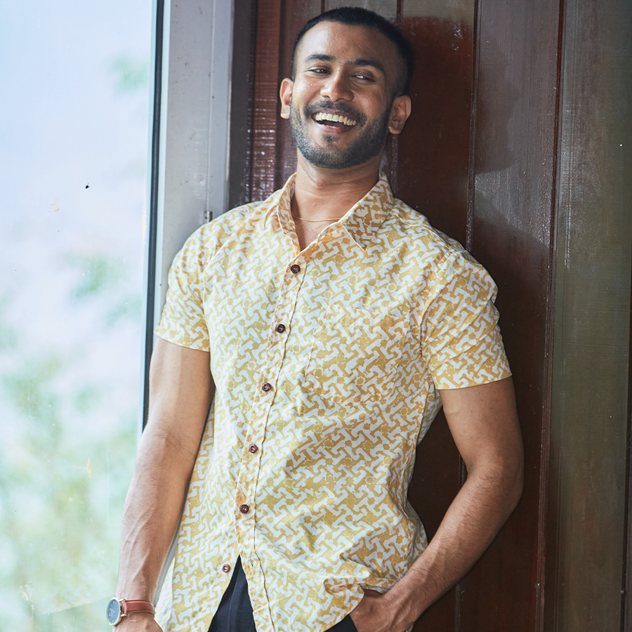 a photo of a man posing happily while leaning on a wooden structure in a batik shirt in the pattern mustard arabesque