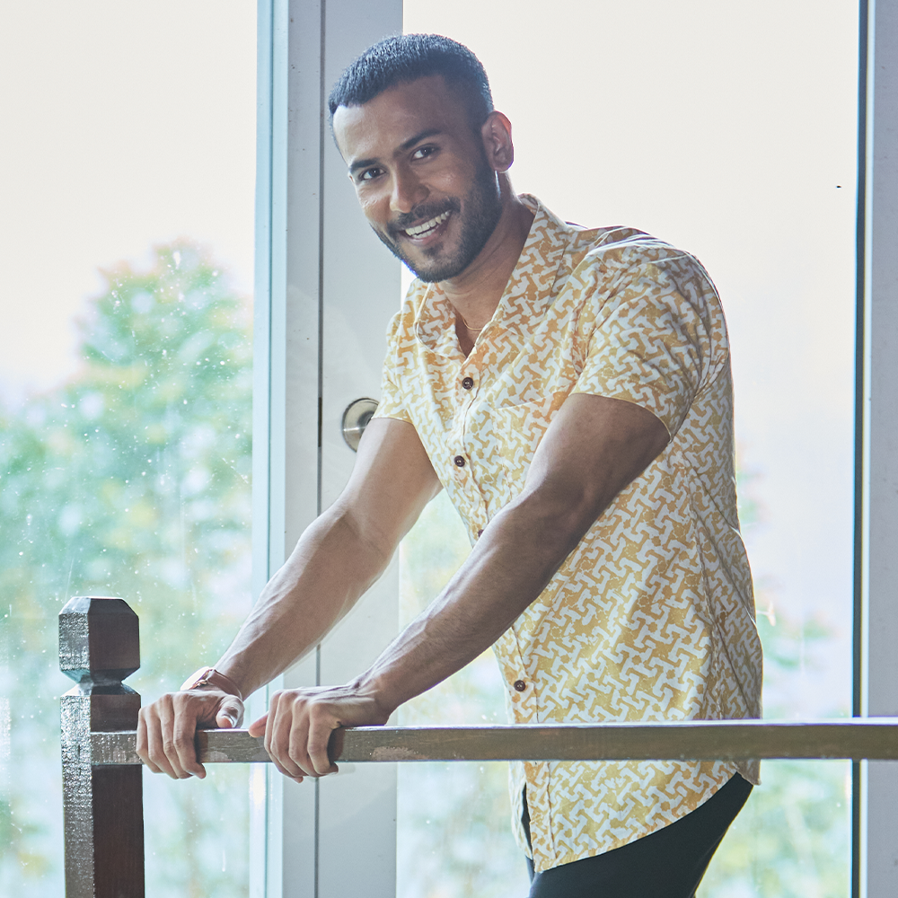 a man leaning against a wooden railing in an genuine batik shirt in the pattern mustard arabesque