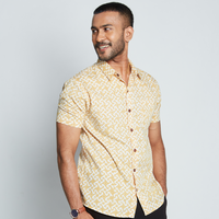 a man wearing a batik shirt in the pattern mustard arabesque against a neutral background