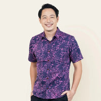 A gentleman elegantly posing in an authentic Purple Bintik patterned batik shirt against a neutral background