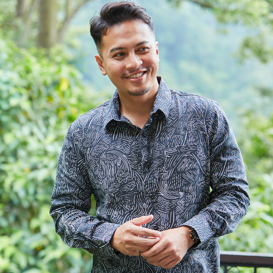 In a captivating lifestyle photograph, a man exudes style and authenticity while wearing a Black Driftwood patterned batik shirt, set against a backdrop of the serene natural world