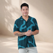 Man wearing a teal patterned shirt against a beige background
