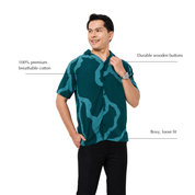 A man modeling a short-sleeve button-up shirt with a teal and dark green abstract wavy pattern, set against a plain white background with text callouts highlighting fabric and features.