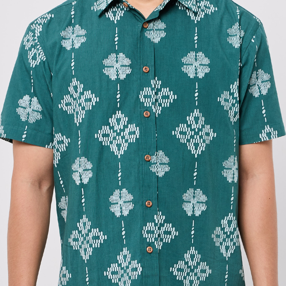 Teal shirt with white geometric pattern worn by a person on a plain background