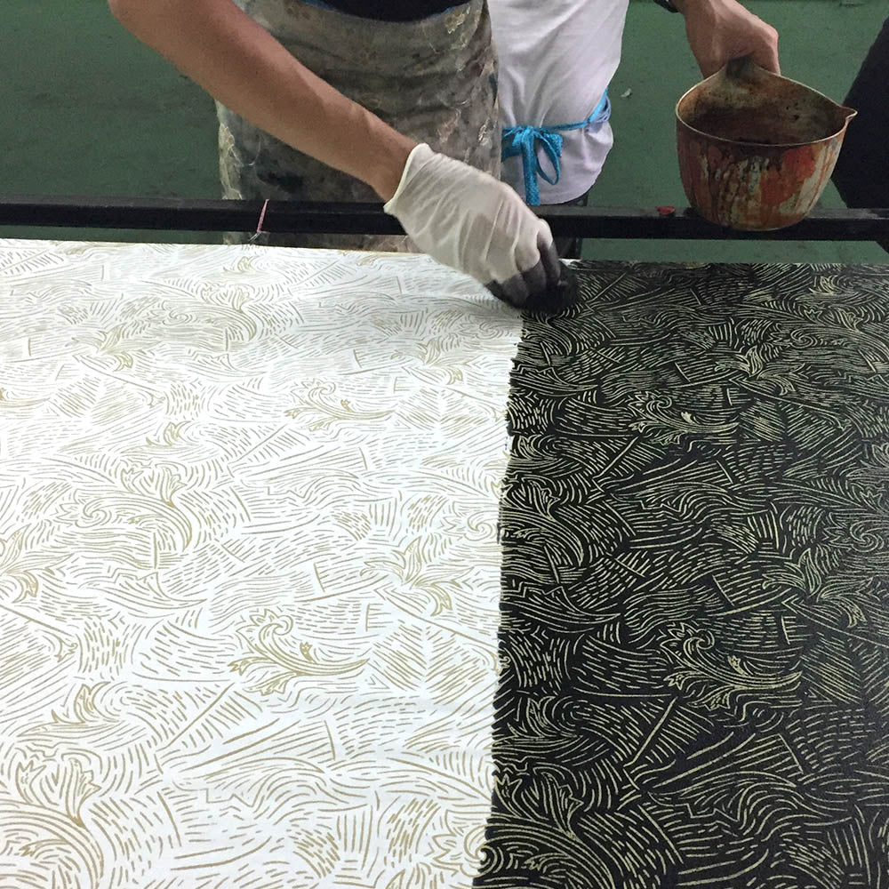 Person applying a patterned design to a large sheet of paper using a tool.