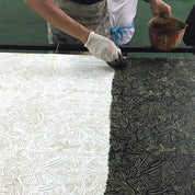 Person applying a patterned design to a large sheet of paper using a tool.