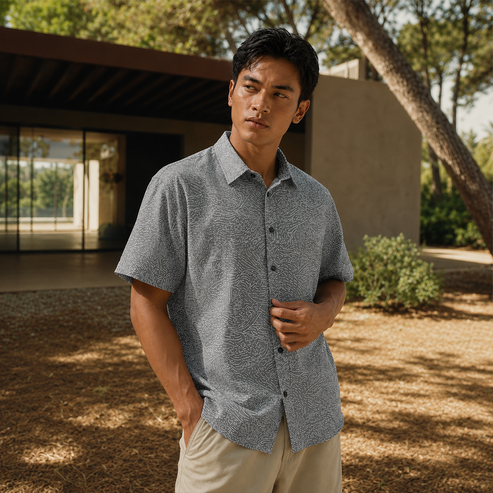 Man wearing a gray patterned shirt and beige pants standing outdoors.