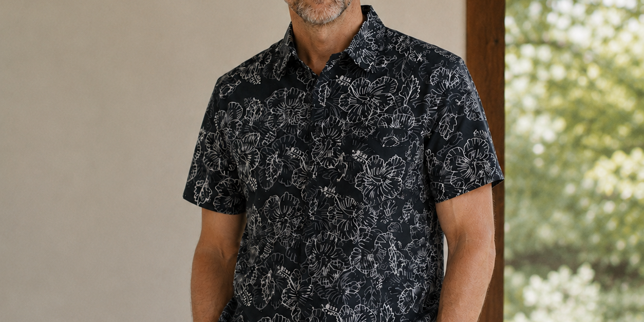 Man wearing black printed batik shirt with hibiscus print, posing indoors while indoors
