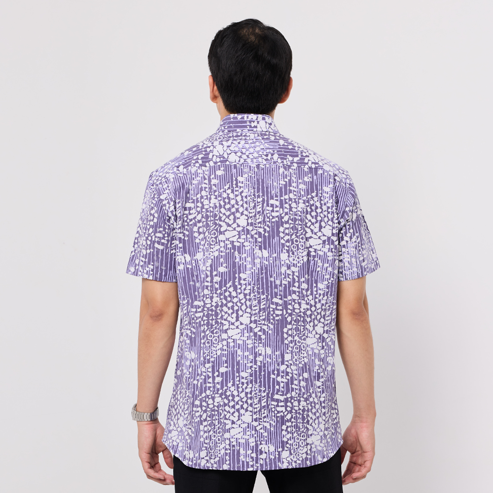 Person wearing a short-sleeve, patterned Batik shirt on a plain background