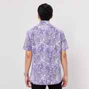Person wearing a short-sleeve, patterned Batik shirt on a plain background