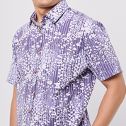 Person wearing a short-sleeve Batik shirt with a purple and white pattern on a plain background