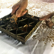 Person handling a lobster in a metal tray on a patterned tablecloth.