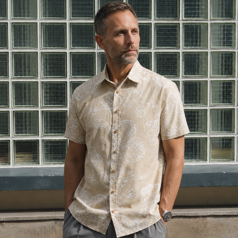 Man wearing tan printed batik shirt, posing outside with his hands in his pockets