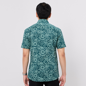 Person wearing a green patterned Batik shirt on a plain background