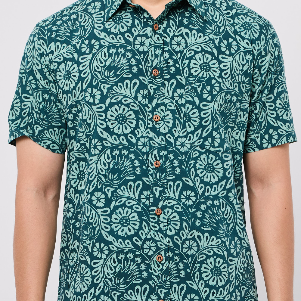 Person wearing a teal patterned Batik shirt on a plain background