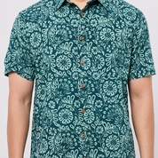 Person wearing a teal patterned Batik shirt on a plain background