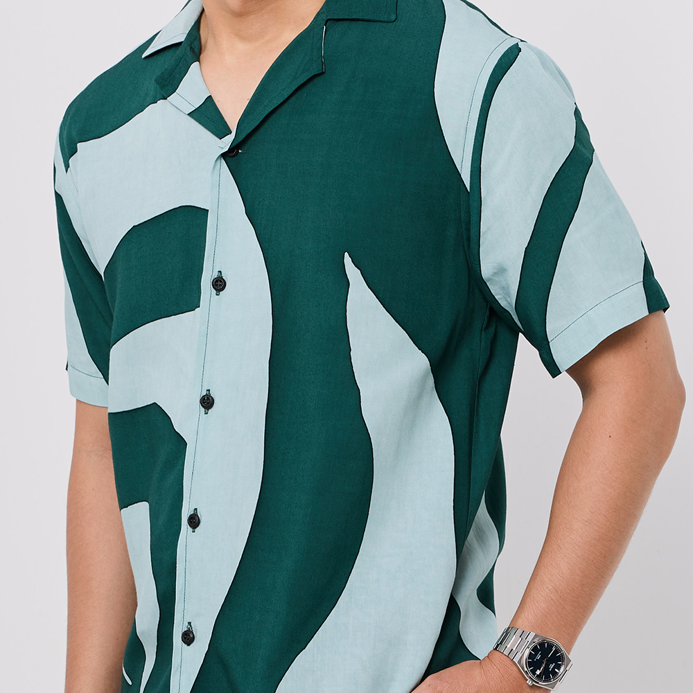 Person wearing a green and light blue patterned shirt on a plain background