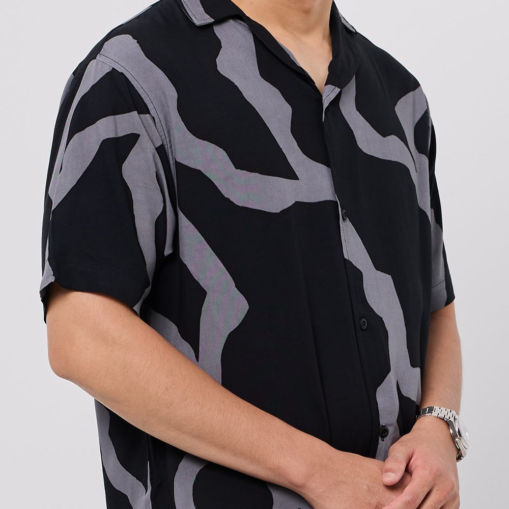Person wearing a black and gray patterned shirt on a plain background