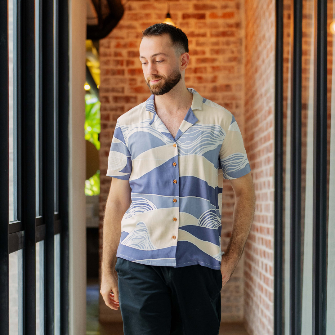 Man wearing a patterned shirt standing in front of a brick wall.