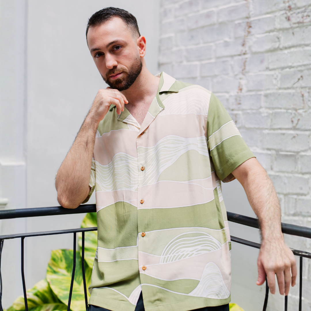 Man wearing a patterned shirt standing against a light brick wall.