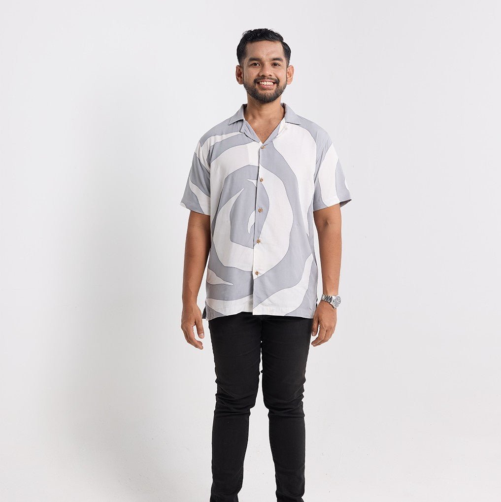 Man wearing a patterned shirt and black pants on a white background