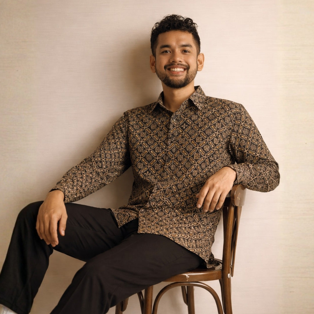 Man sitting on a chair wearing a patterned batik shirt against a beige wall