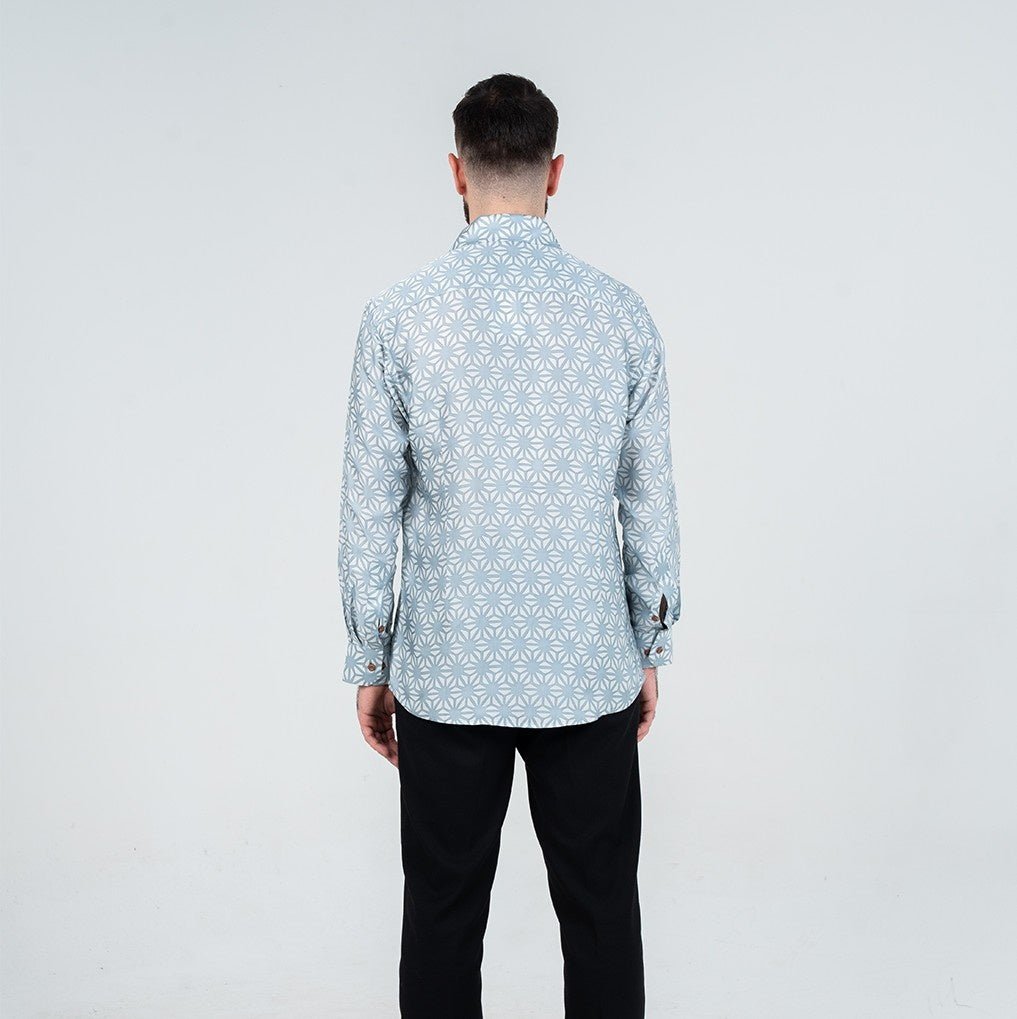 Man wearing a light blue patterned shirt and black pants on a white background