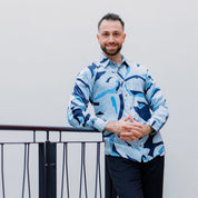 Man wearing a blue and white patterned shirt standing against a plain background