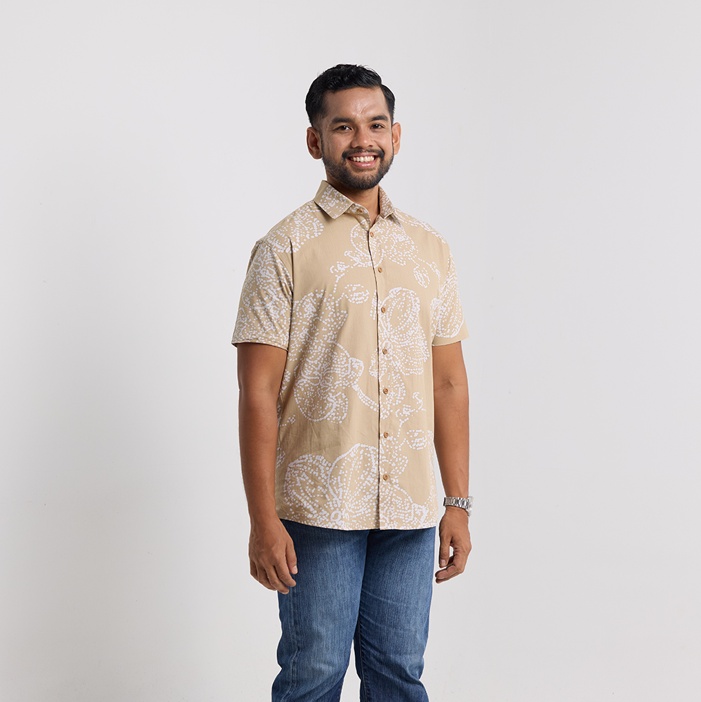 Man wearing a beige patterned shirt and blue jeans on a white background