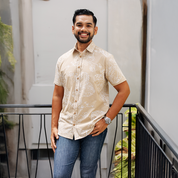 Man wearing a beige patterned shirt and blue jeans standing on a balcony.