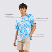 Man wearing light blue printed batik shirt with shell-like prints posing with hand in his pocket and annotated details by his sides