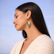 Woman wearing gold leaf-shaped earrings against a blue sky background