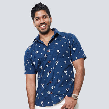 a man standing in front of a white wall wearing a batik shirt in navy palm pattern
