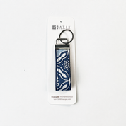 A vertical keychain with a navy blue and white patterned fabric strap and a silver metal split ring, in its packaging shown on a plain white background.
