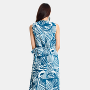 A woman viewed from the back wearing a sleeveless wrap-style dress with a bold blue and white abstract pattern, set against a plain light gray studio background.